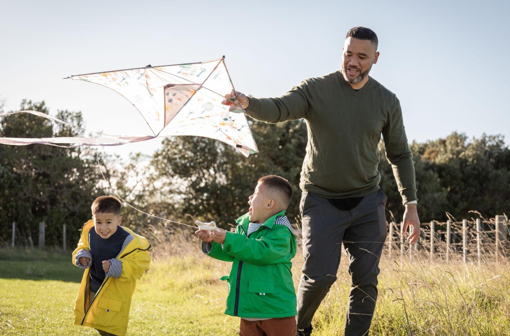 Father flying a kite outdoors with his two young sons on a sunny day
