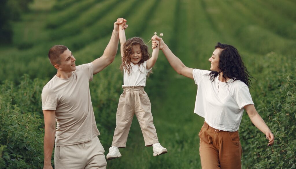 Parents playfully lifting their child by the hands during a family walk outdoors, celebrating joyful moments of parenting.